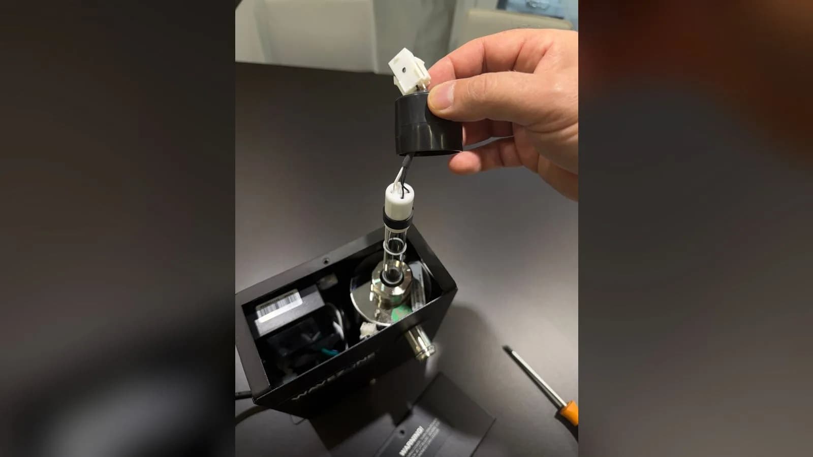 Main qui tire le capuchon noir vers le haut : la lampe UV en verre sort tout droit de son logement chromé dans le boîtier Wavezone